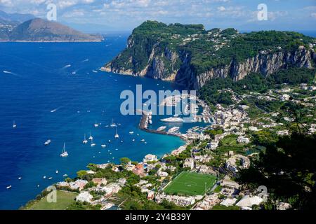 Blick aus der Vogelperspektive auf die atemberaubende Küste von Capri, Italien, mit den zerklüfteten Klippen, dem blauen Meer und dem geschäftigen Yachthafen mit Booten. Stockfoto