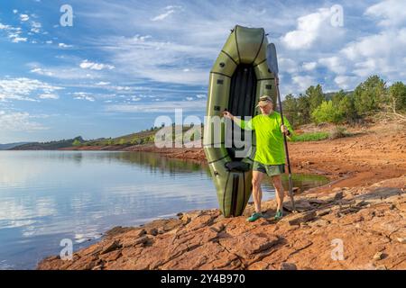 Senior männlicher Paddler startet ein aufblasbares Packboot an einem Ufer des Horsetooth Reservoir in Colorado Stockfoto