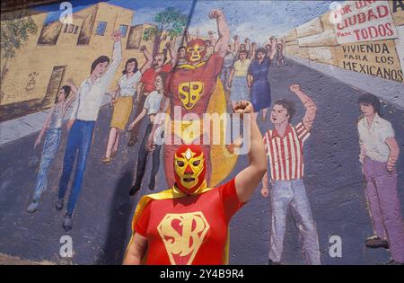 Mexiko, Mexiko-Stadt. Super Bario posiert vor einem Wandbild von sich selbst. Super Bario ist ein Held von Lucha libre, einem mexikanischen Wrestling-Spiel. Stockfoto