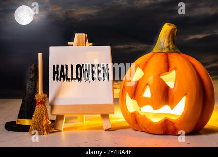 16. September 2024: Eine leuchtende Kürbislaterne neben einem Brett mit der Inschrift Halloween, flankiert von Hexenhut und Besen. Im Hintergrund scheint der Vollmond durch eine düstere Wolkendecke und schafft so eine typische Halloween-Atmosphäre. FOTOMONTAGE *** eine leuchtende Kürbis-Laterne neben einer Tafel mit der Aufschrift: Halloween, flankiert von einem Hexenhut und Besen. Im Hintergrund leuchtet der Vollmond durch eine düstere Wolkendecke, was eine typische Halloween-Stimmung schafft. FOTOMONTAGE Stockfoto
