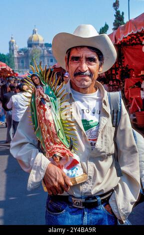 Mexiko, Mexiko-Stadt. Mann mit der Statue der Jungfrau Maria auf dem Platz vor der Basilika - alt und neu - unserer Lieben Frau von Guadalupe. Stockfoto