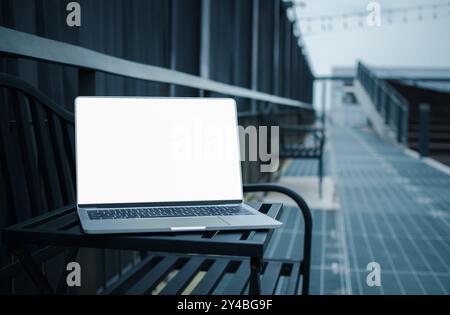 Laptop mit leerem weißen Bildschirm auf einem Metalltisch neben dem Flur in einer modernen Stadt, leerer Kopierraum, leerer Bildschirm-Mockup, Soft Focus Laptop Stockfoto