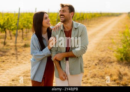 Fröhliches Paar lacht und umarmt sich unter der warmen Sonne in einem malerischen Weinberg, umgeben von Reihen von lebhaften Weinreben und goldener Erde Stockfoto