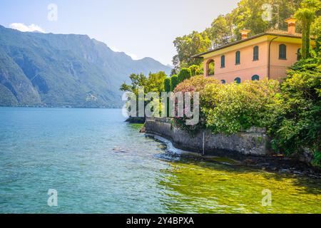 Ein friedlicher Blick auf den Comer See mit üppigem Grün und einer bezaubernden Villa am Wasser. Das Sonnenlicht schimmert auf der Oberfläche und verstärkt die ruhige Atmosphäre. Stockfoto