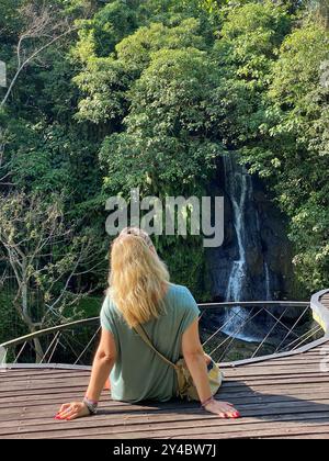 Das blonde Mädchen sitzt und beobachtet den Layana-Wasserfall in Ubud an sonnigen Tagen. Stockfoto
