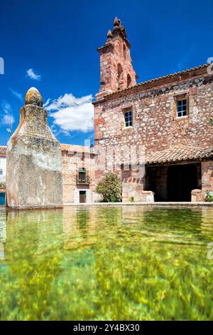 Neben einem historischen Gebäude in La Barbolla befindet sich ein ruhiger Trinktrog mit klarem Wasser, das den leuchtend blauen Himmel und die Umgebung reflektiert. Stockfoto