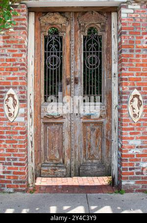Antike Doppeltür, umgeben von Ziegelsteinen mit dekorativen Einsätzen. Die Tür ist verwittert und hat vergitterte Fenster Stockfoto