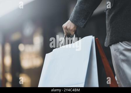 Nahaufnahme eines jungen kaukasischen Mannes, der auf der Straße ein paar Papiereinkaufstaschen hält Stockfoto
