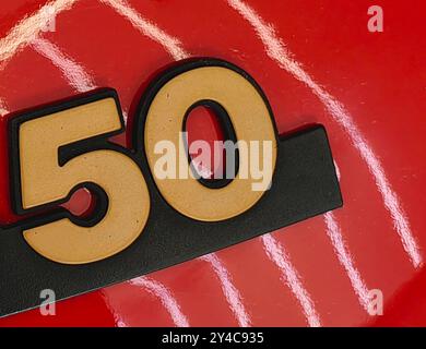 Goldene Zahl 50 auf roter Oberfläche mit Reflexion des weißen Neonlichts. Stockfoto