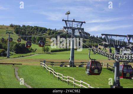 Seilbahnbahnen fahren über grüne Wiesen in einer bergigen Landschaft unter klarem blauen Himmel, willingen, sauerland, deutschland Stockfoto