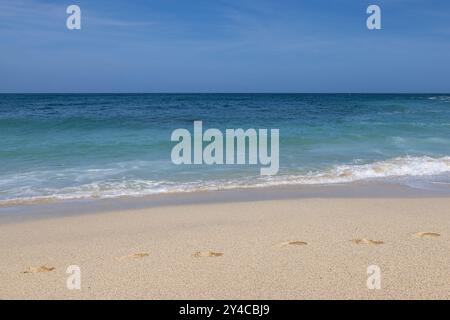 Ein idyllischer Sandstrand in Cornwall, mit Fußspuren im Sand und einem blauen Himmel darüber Stockfoto