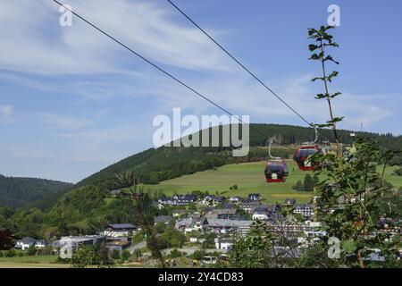 Zwei Seilbahnkabinen, die über einer hügeligen Landschaft mit Häusern und Wäldern schweben, willingen, sauerland, deutschland Stockfoto