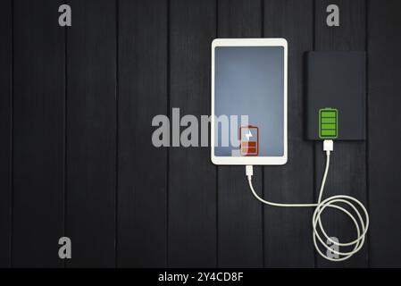 Powerbank lädt Tablet-PC, Smartphone, isoliert auf hölzernem Hintergrund. Ladekonzept. Freier Copyspace Stockfoto