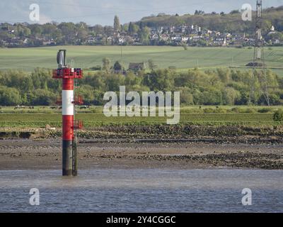 Nahaufnahme eines rot-weißen Leuchtturms an einem flachen Ufer vor einer grünen Landschaft, themse. tilbury, England, Großbritannien Stockfoto