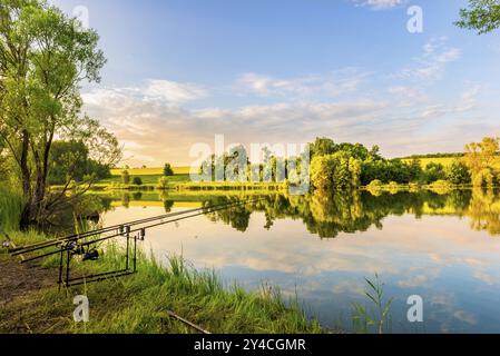 Angelruten an einem Ufer des ruhigen Flusses bei Sonnenuntergang Stockfoto