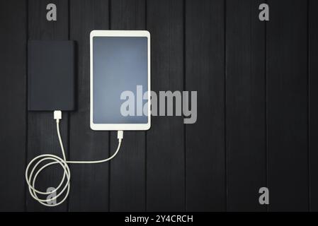 Powerbank lädt Tablet-PC, Smartphone, isoliert auf hölzernem Hintergrund. Ladekonzept. Freier Copyspace Stockfoto