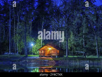 Holz- Haus in conifurous Wald in der Nähe von Teich bei Nacht Stockfoto