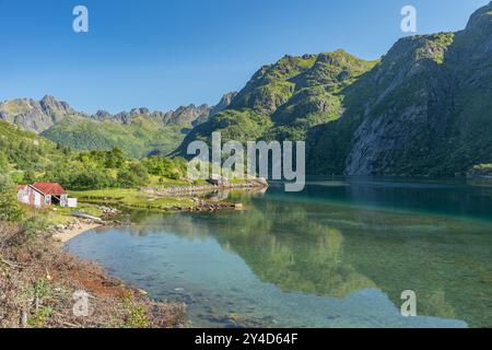 Kristallklarer See in der Nähe von Bergen mit Reflexionen auf dem Wasser mit verlassenem Haus an der Küste, Lofoten Norwegen Stockfoto