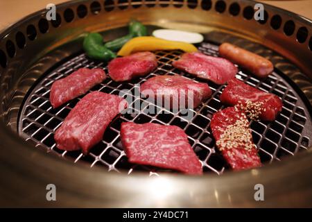 Eine Nahaufnahme erstklassiger Wagyu-Rindfleischscheiben, die auf einem traditionellen japanischen Yakiniku-Grill gegrillt werden. Stockfoto