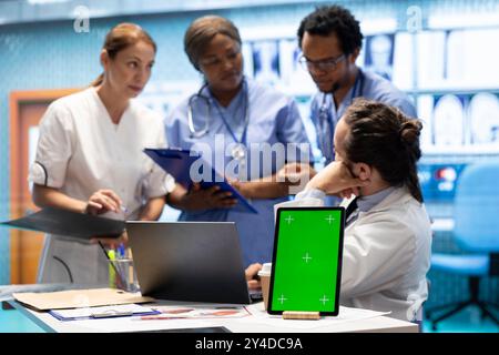 Gruppe von Ärzten, die Krankenhausaufzeichnungen neben der Chroma Key-Anzeige konsultieren und die Diagnose anhand der Ergebnisse des Röntgentests untersuchen. Verschiedene Experten treffen sich in einer Privatklinik, um einen Behandlungsplan zu erstellen. Stockfoto