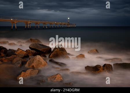 In diesem mit Langzeitbelichtung aufgenommenen Bild erreichen die Meereswellen den Strand vor der Pont del Petroli (Ölbrücke) in Badalona, nördlich von Barcelona. Stockfoto