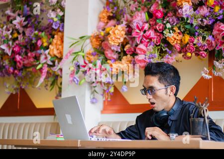 Asiatischer gutaussehender männlicher Student schockiert, dass Laptop-Online-Bestellung nicht auf dem Tisch bearbeitet wurde, und in einem Café sitzt, in dem er arbeitet. Für Unternehmensinhalte, fa Stockfoto