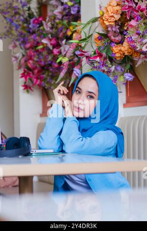 Porträt eines schönen jungen asiatischen Mädchens mit elegantem Kopftuch und Händen parallel zum Kinn in einem Café. Für Werbung Stockfoto