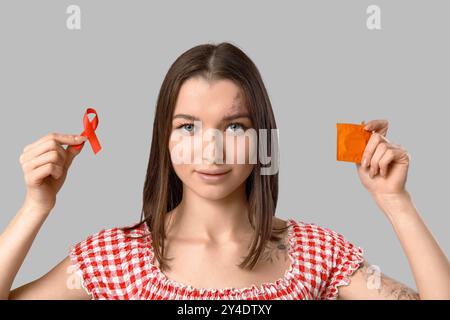 Schöne junge Frau mit Kondom und rotem Band auf grauem Hintergrund. AID Awareness-Konzept Stockfoto