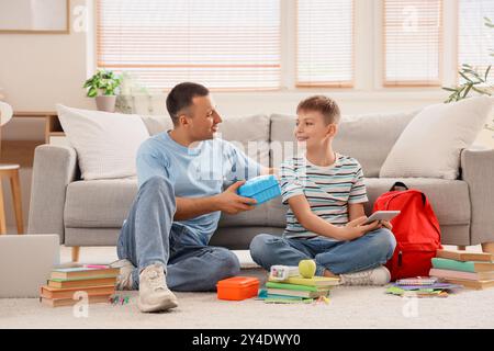 Vater mit Schulbrotdose und sein kleiner Sohn packt zu Hause den Rucksack Stockfoto