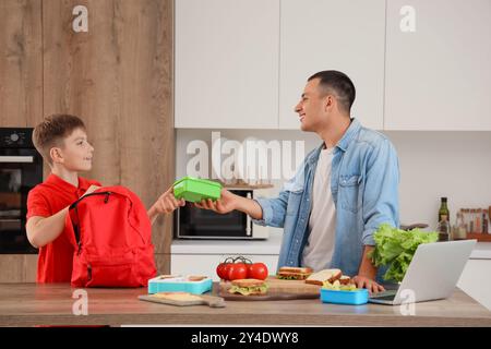 Ein kleiner Junge mit seinem Vater packt in der Küche die Lunchbox der Schule in den Rucksack Stockfoto