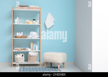 Modernes Regal mit Badaccessoires und Hocker in der Nähe der blauen Wand im Zimmer Stockfoto