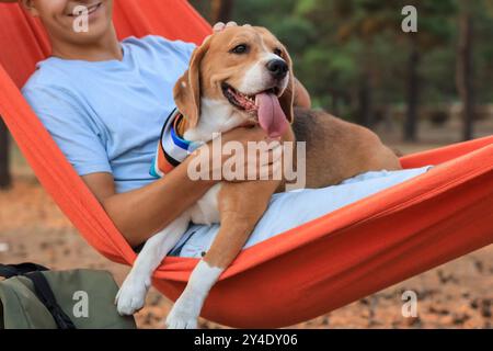 Junger Mann mit Beagle-Hund, der draußen in einer roten Hängematte ruht Stockfoto