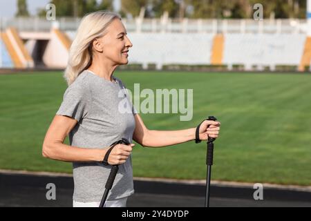 Schöne reife glückliche Frau, die mit Gehstöcken im Stadion trainiert Stockfoto