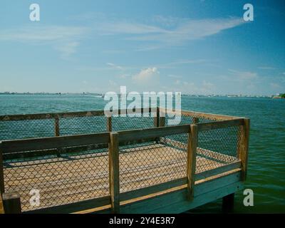 Weiter Blick über den Holzsteg Pier über die Boca Ciega Bay in Gulfport, FL. Hellblauer Himmel mit weißen Wolken und ruhigem Wasser. Boot nähert sich Stockfoto