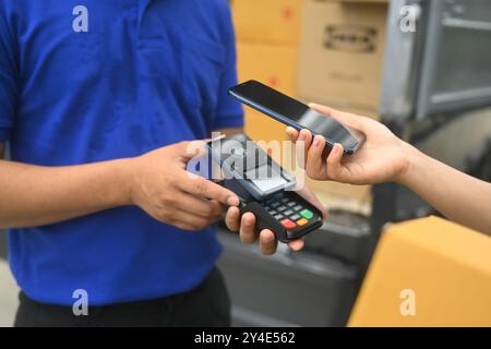 Frau, die kontaktlos mit dem Smartphone an den Liefermann bezahlt. Digitale Zahlungen und modernes Einkaufskonzept Stockfoto