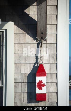 Vintage-Hummerboje rot-weiß mit dem roten kanadischen Ahornblatt, der kanadischen Flagge, hängt vor dem Büro des Hafenmeisters an der Market Wharf in der Passamaquoddy Bay im Zentrum von Saint Andrews, New Brunswick, Kanada. Stockfoto