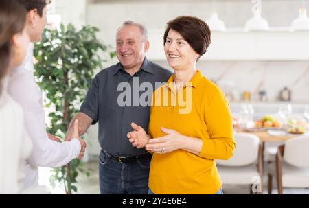 Ältere Eltern mit offenen Armen begrüßen den Sohn mit seiner Frau zu Hause Stockfoto