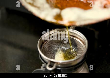 Goldene geklärte Butter, die sorgfältig durch ein Sieb gesiebt wird, fängt die Essenz kulinarischer Präzision ein. Stockfoto