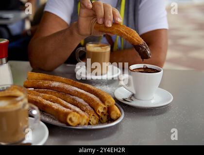 Die Frau hält Churros in der Hand. Churros beliebte köstliche spanische Küche mit heißer Schokolade, Zucker und Kaffee auf dem Restauranttisch Stockfoto