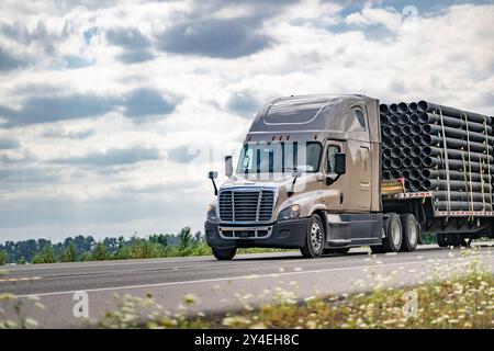 Industrieller Langstreckenwagen beige, großer Lkw-Auflieger mit Treppenauflieger für den Transport befestigter Kunststoffrohre auf der Sommerautobahn Stockfoto