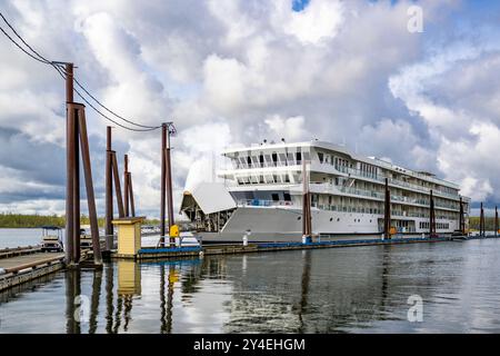 Die Wasserlandschaft des großen Passagier-Flussschiffes, das an einem Flusspier ankert, dessen Bug geöffnet ist, um Fracht zu laden und die Vorräte für den Rest des Schiffes aufzufüllen Stockfoto