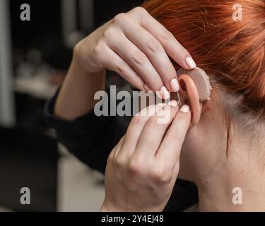 Kaukasische Frau, die im Büro ein Hörgerät auflegt. Stockfoto