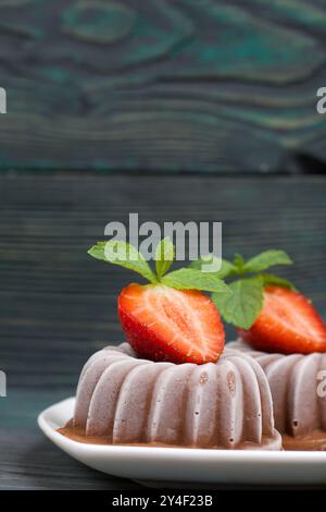 Schokoladenfudge garniert mit einer halben Erdbeere mit Blütenblättern. Untertasse mit Nachtisch auf Brettern aus gebürstetem Kiefernholz in Schwarz und Grün. Stockfoto