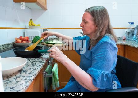 Frau über 60 Jahre alt im Rollstuhl, die zu Hause kocht. Behinderte Frau Stockfoto