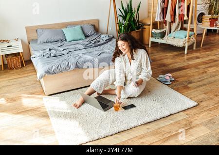 Eine junge Frau in Übergröße entspannt sich auf einem weichen Teppich, während sie zu Hause an ihrem Laptop arbeitet. Stockfoto