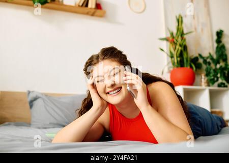 Eine fröhliche Frau in Übergröße genießt einen unbeschwerten Moment, lacht am Telefon, während sie sich auf ihrem gemütlichen Bett entspannt. Stockfoto