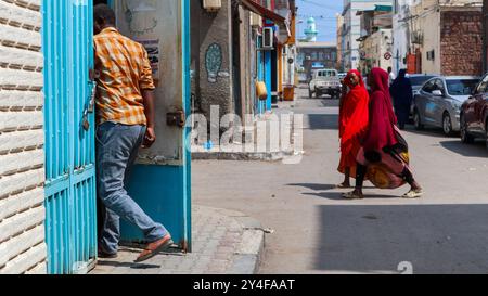 Dschibuti: Atmosphäre in der Altstadt, verschleierte Frauen in traditioneller Kleidung überqueren die Straße. Im Hintergrund das Minarett der Hamoudi-Moschee Stockfoto