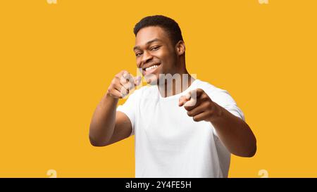 Glücklicher schwarzer Mann, der dich vor orangefarbenem Hintergrund wählt Stockfoto