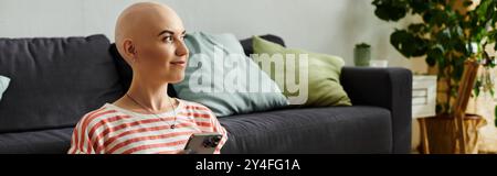 Eine ruhige junge Frau mit Alopezie lächelt, während sie ihr Smartphone drinnen benutzt. Stockfoto