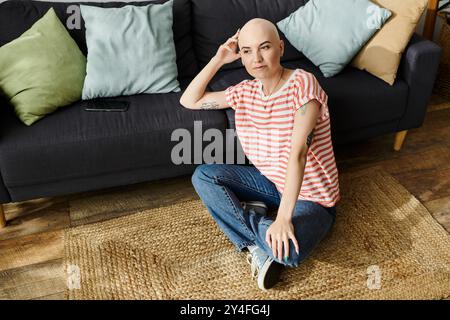 Eine junge kahlköpfige Frau sitzt bequem auf dem Boden und reflektiert sich in einem warmen, einladenden Raum. Stockfoto